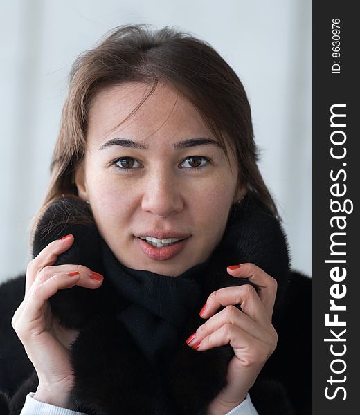 Pretty lady adjusting her fur coat' collar - portrait on gray background