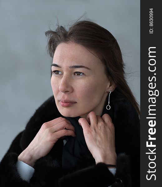 Pretty lady adjusting her fur coat' collar - portrait on gray background