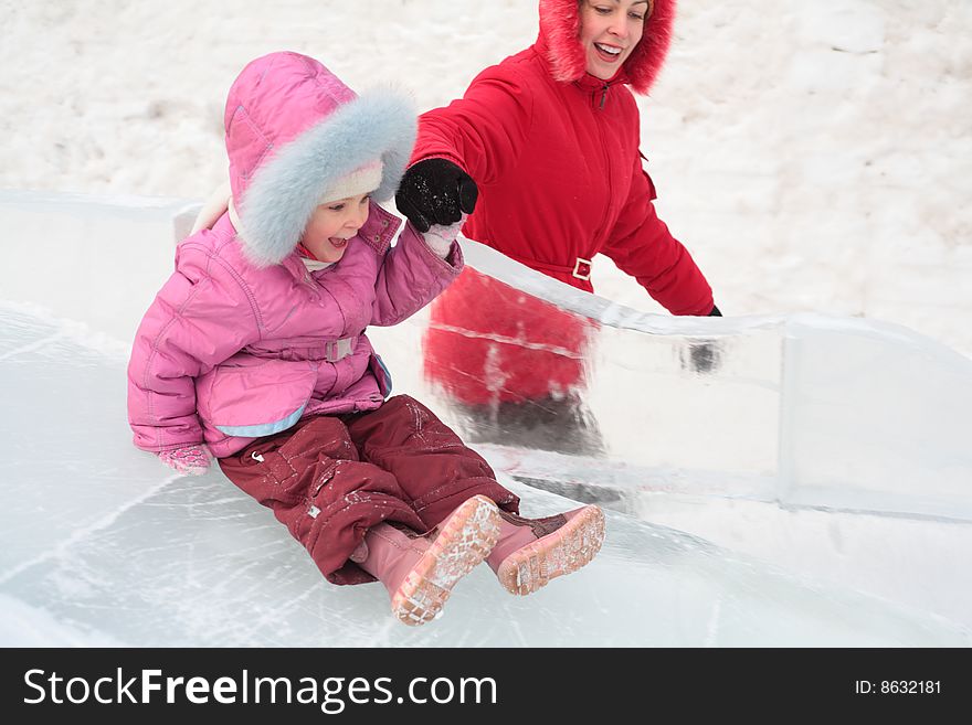 Little girl rolls down on ice slope with mother