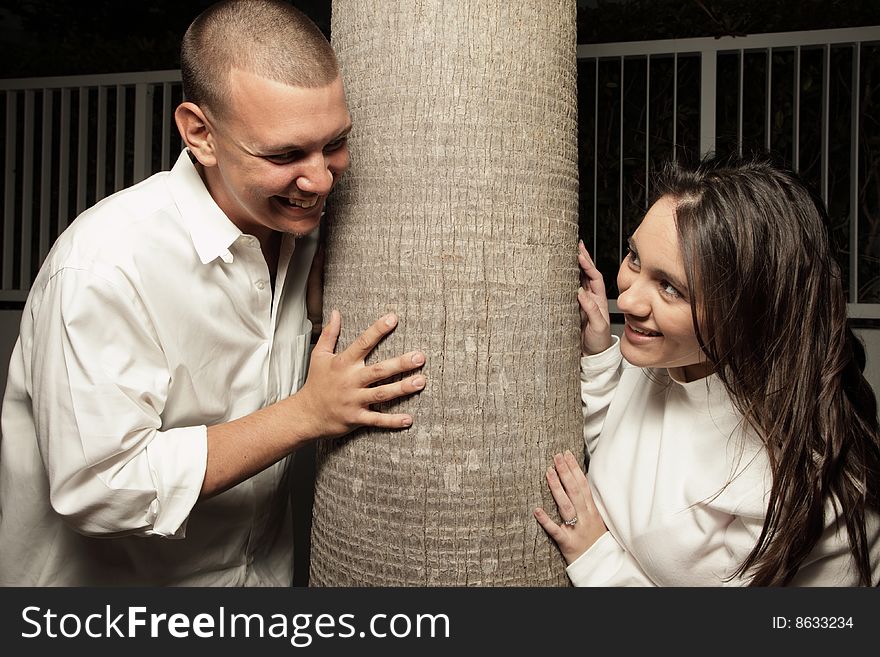 Young couple smiling with a tree in between them. Young couple smiling with a tree in between them