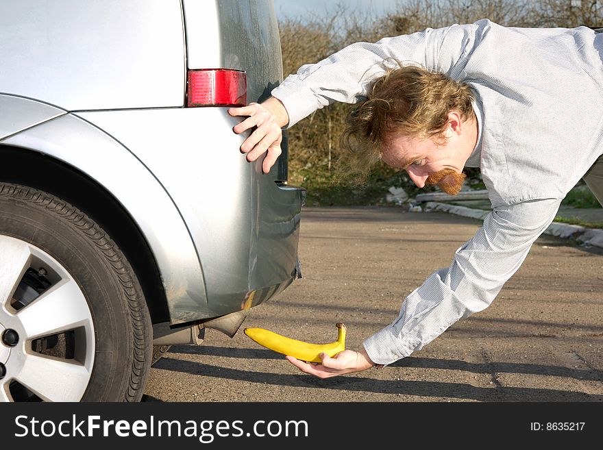 Man putting banana into car exhaust pipe. Man putting banana into car exhaust pipe