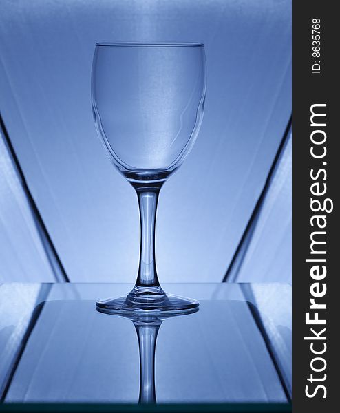 The blue wine glass whith reflection on a glass background. The blue wine glass whith reflection on a glass background