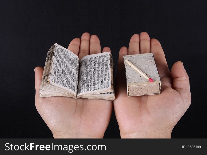 A mini book and matchbox contrast on hand over black background