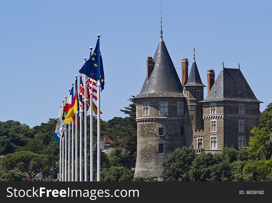 Ten flags on flag poles adjacent to a French chateau surrounded by trees, set against a blue summer sky. Horizontal Orientation. Ten flags on flag poles adjacent to a French chateau surrounded by trees, set against a blue summer sky. Horizontal Orientation