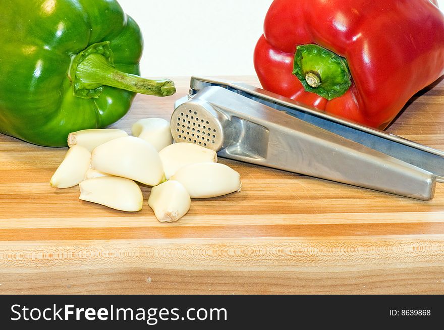 Whole red and green pepper on a wooden cutting board with garlic cloves and a garlic press. Whole red and green pepper on a wooden cutting board with garlic cloves and a garlic press.