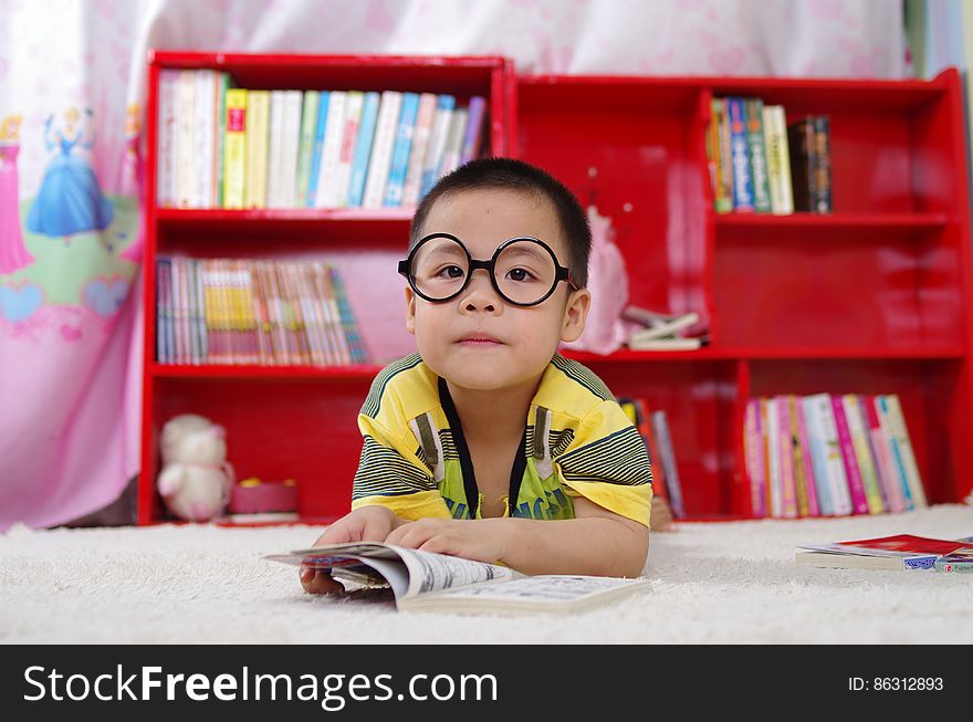 Young boy wearing glasses laying on floor reading book. Young boy wearing glasses laying on floor reading book