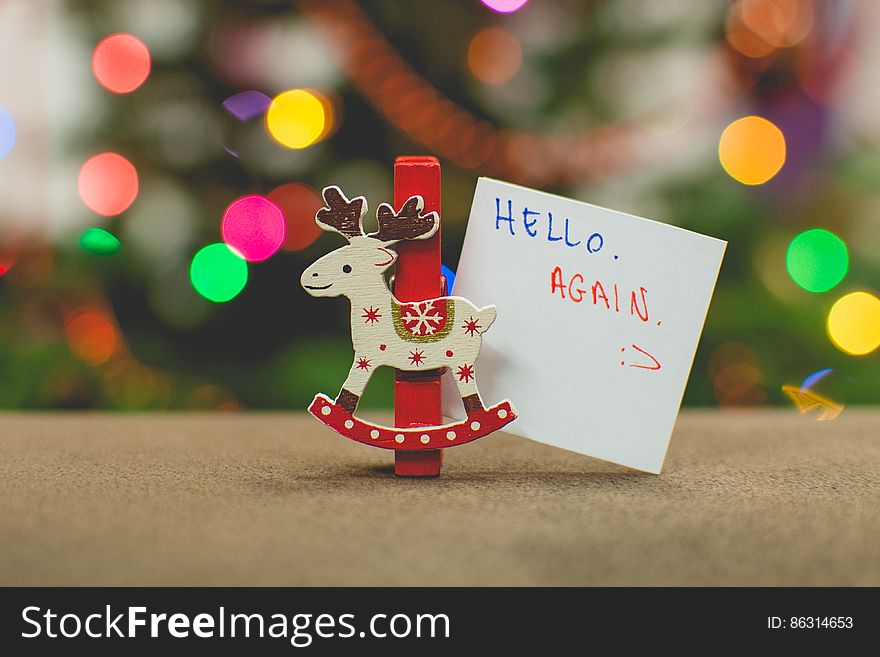 Reindeer Christmas ornament with small sign saying hello again against colorful bokeh lights. Reindeer Christmas ornament with small sign saying hello again against colorful bokeh lights.