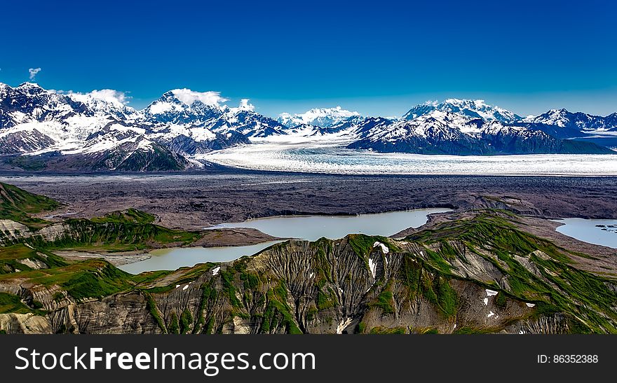 Glacial mountain landscape with melting pools on sunny day with blue skies.