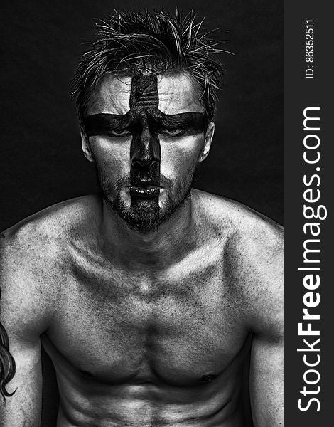 Portrait of man without shirt wearing cross in paint on face in black and white. Portrait of man without shirt wearing cross in paint on face in black and white.