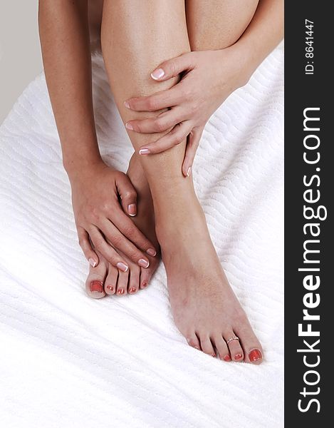 A young woman sitting on the floor on a white towel shooing her legs and the feet with red toenails, with her hands on the legs. A young woman sitting on the floor on a white towel shooing her legs and the feet with red toenails, with her hands on the legs.