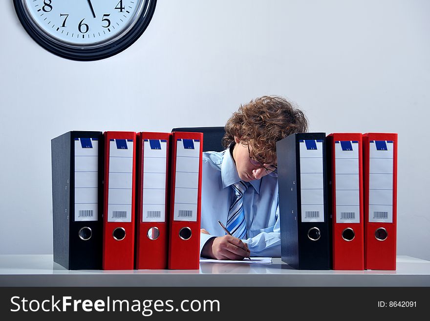 Young businessman standing at desk behind a stack of folders. Young businessman standing at desk behind a stack of folders