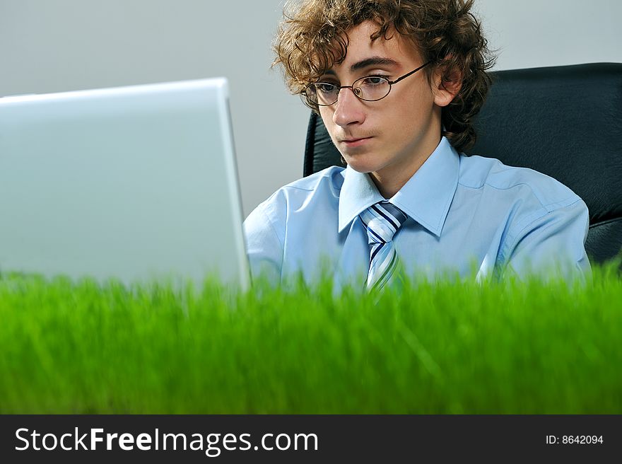 Young businessman using laptop on a desk with grass. Young businessman using laptop on a desk with grass