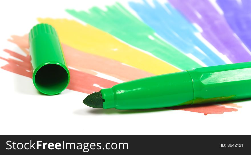 Green felt-tip pen with removed cap on a background of the drawn rainbow close-up