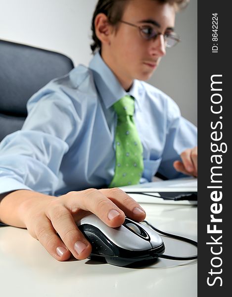 Young businessman at desk handling mouse, focus on mouse. Young businessman at desk handling mouse, focus on mouse