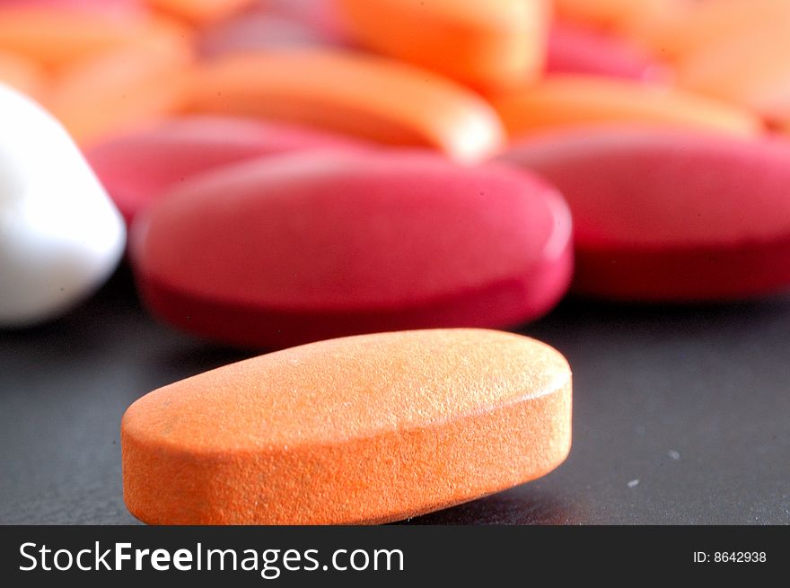 A close-up image of an orange pill with many pills behind it. A close-up image of an orange pill with many pills behind it.