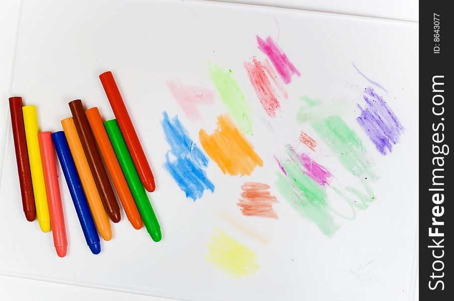 Eight oil pencils on a white plastic board with traces of drawing
