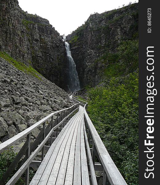 A wooden walkpath leading to a waterfall.