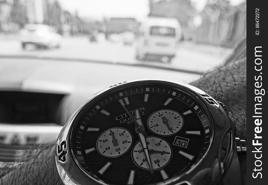 Close up of Citizen quartz watch with precise timing facility on the arm of a driver of a car, with background through windscreen of blurred image of the road and traffic. Close up of Citizen quartz watch with precise timing facility on the arm of a driver of a car, with background through windscreen of blurred image of the road and traffic.