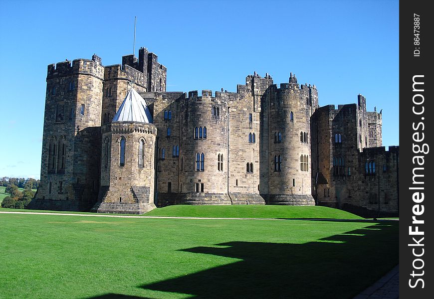Exterior of Alnwick Castle in Northumberland, England on green lawn on sunny day with blue skies. Exterior of Alnwick Castle in Northumberland, England on green lawn on sunny day with blue skies.