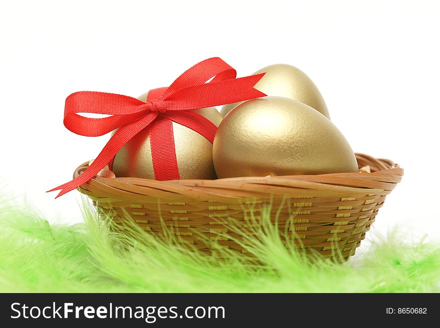 Golden egg wrapped around with red ribbon in basket on green feathers. Golden egg wrapped around with red ribbon in basket on green feathers.