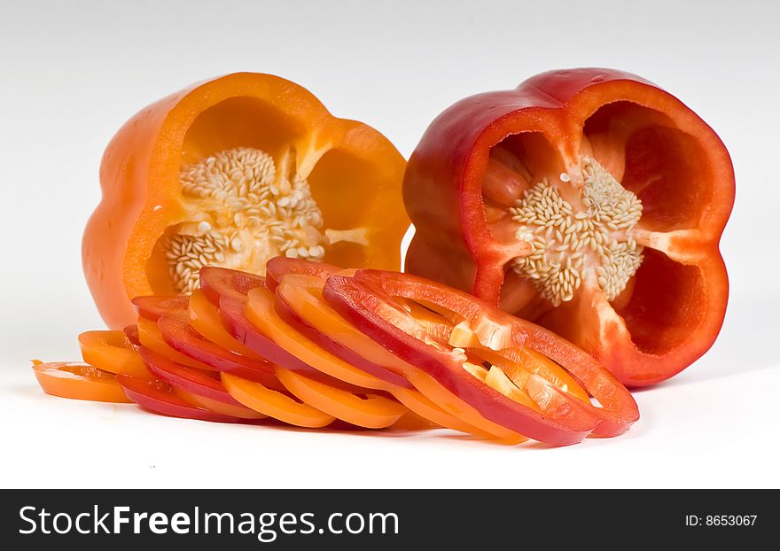 Cut orange and red sweet peppers showing seeds with slices on white