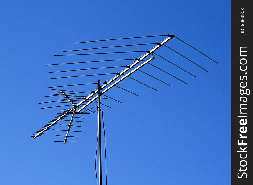 Old fashion aerial television antenna isolated against blue sky.