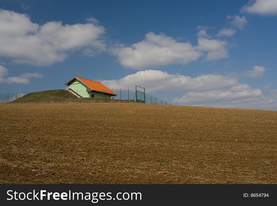 The small green isolated building in the middle of field