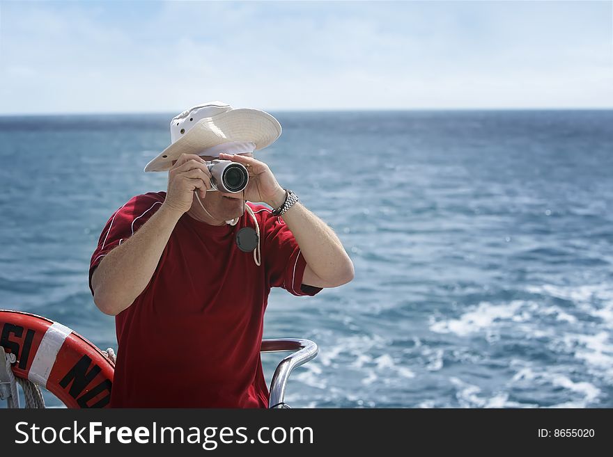 A middle aged man takes photos from a boat. A middle aged man takes photos from a boat