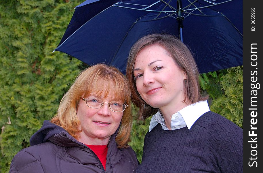 Mother and adult daughter share a moment under an umbrella together. Mother and adult daughter share a moment under an umbrella together.