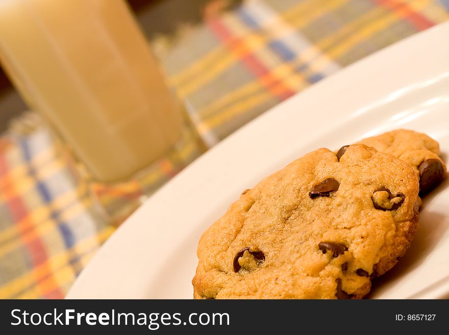 Chocolate chip cookies on a white plate in front of a glass of milk