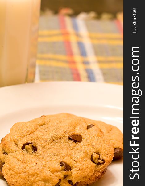 Chocolate chip cookies on a white plate in front of a glass of milk