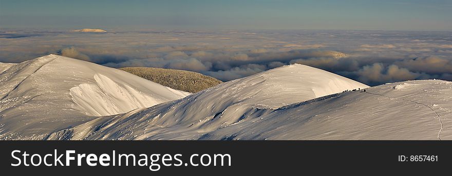 A group of mountaineers in winter are climbing in the Carpathian Mountains at sunset with clouds underneath. A group of mountaineers in winter are climbing in the Carpathian Mountains at sunset with clouds underneath