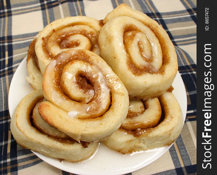 A pile of fresh cinnamon buns on a plate covered with a sugar glaze