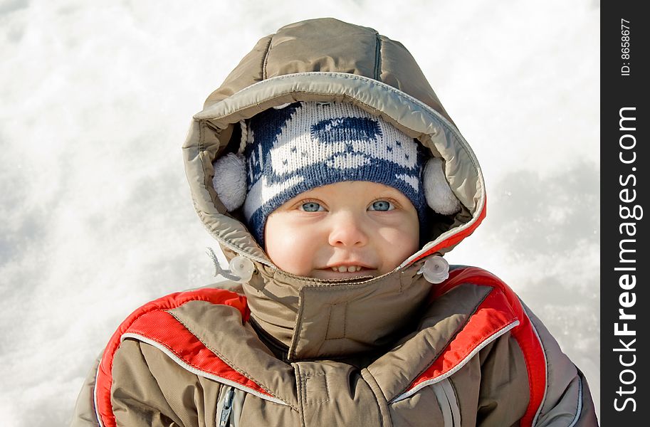 Little boy in winter clothes, against snow, mysteriously smiles. Little boy in winter clothes, against snow, mysteriously smiles