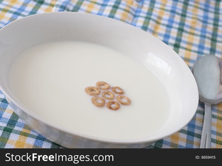 Economy breakfast with a few pieces of cereal floating on milk in a white cereal bowl. Economy breakfast with a few pieces of cereal floating on milk in a white cereal bowl