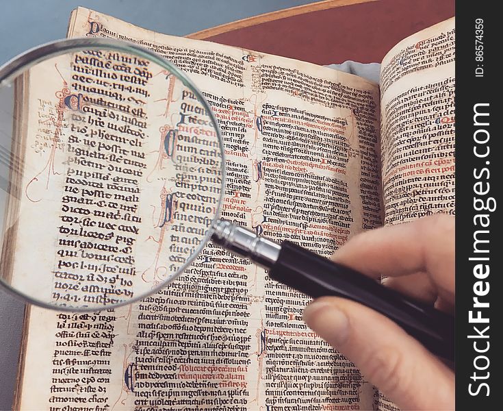 Hand holding magnifying glass over page of antique book. Hand holding magnifying glass over page of antique book.