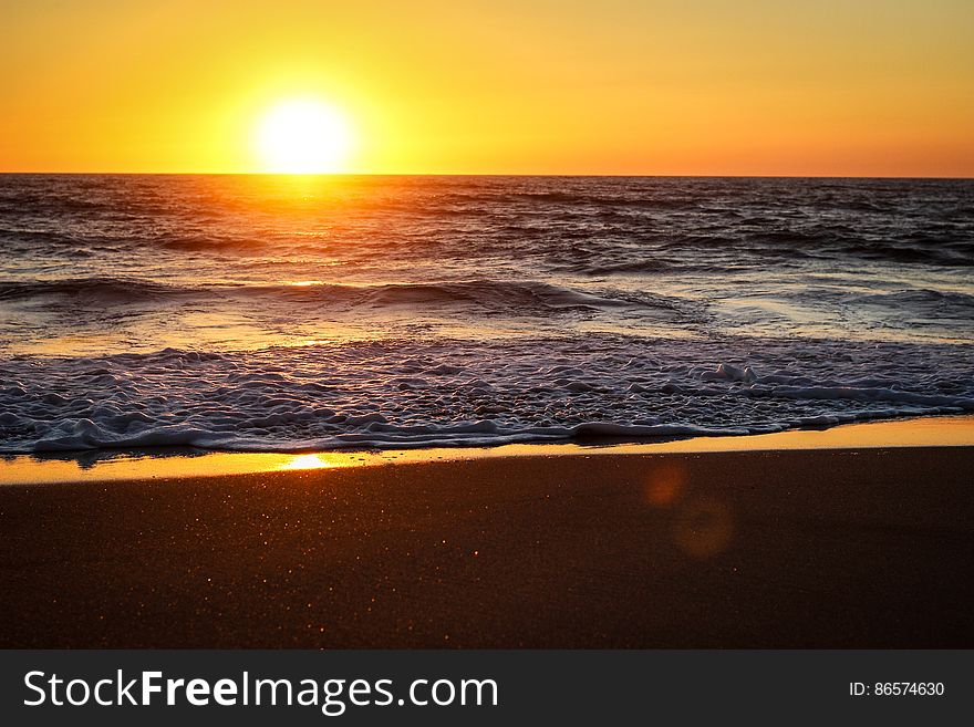 Sunset over horizon along sandy beach with washing waves. Sunset over horizon along sandy beach with washing waves.