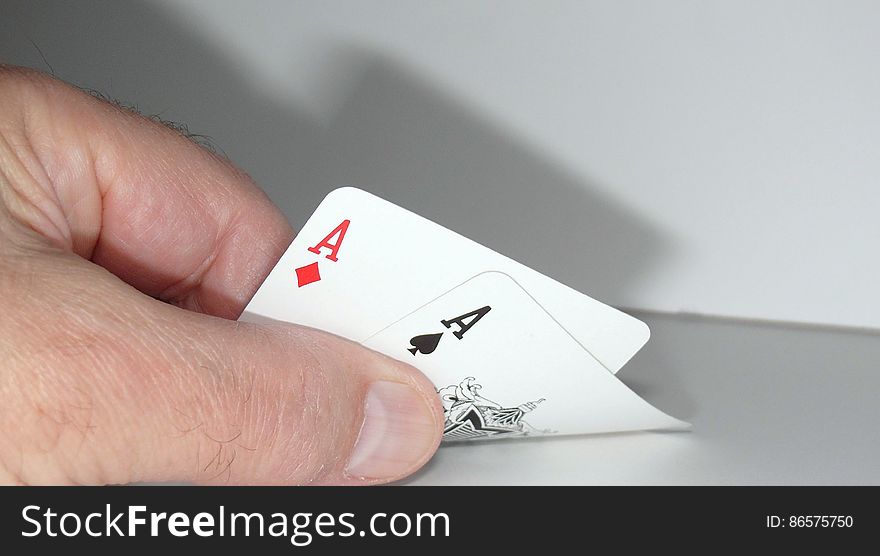 Close up of hand holding pair of aces on desk.