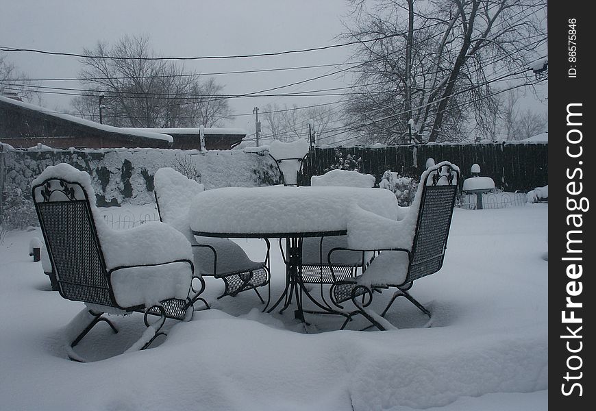 Snow covered patio table and chairs in back yard on overcast day. Snow covered patio table and chairs in back yard on overcast day.