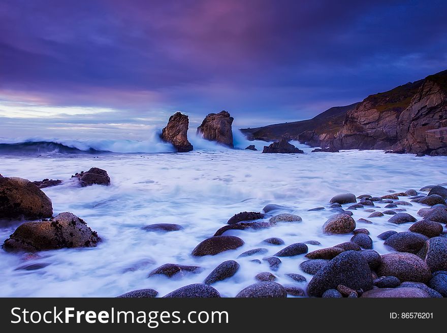 Soft blur of waves washing over rocky shores at dawn with purple skies. Soft blur of waves washing over rocky shores at dawn with purple skies.