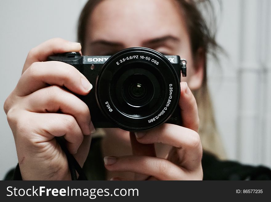 Woman Holding Black Sony Dslr Camera Taking A Photo Of Herself At Mirror