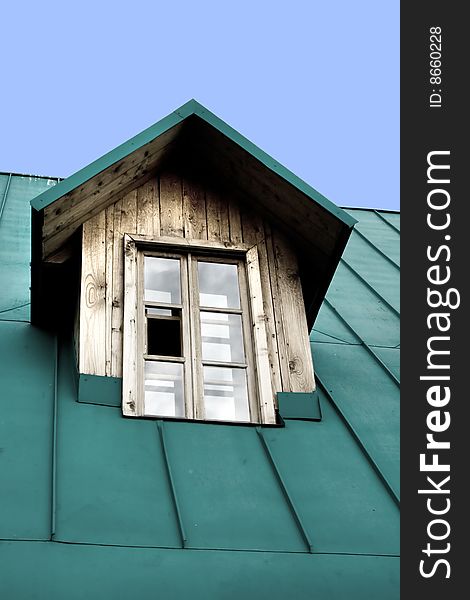 A window on top of a wooden house with a green roof. A window on top of a wooden house with a green roof