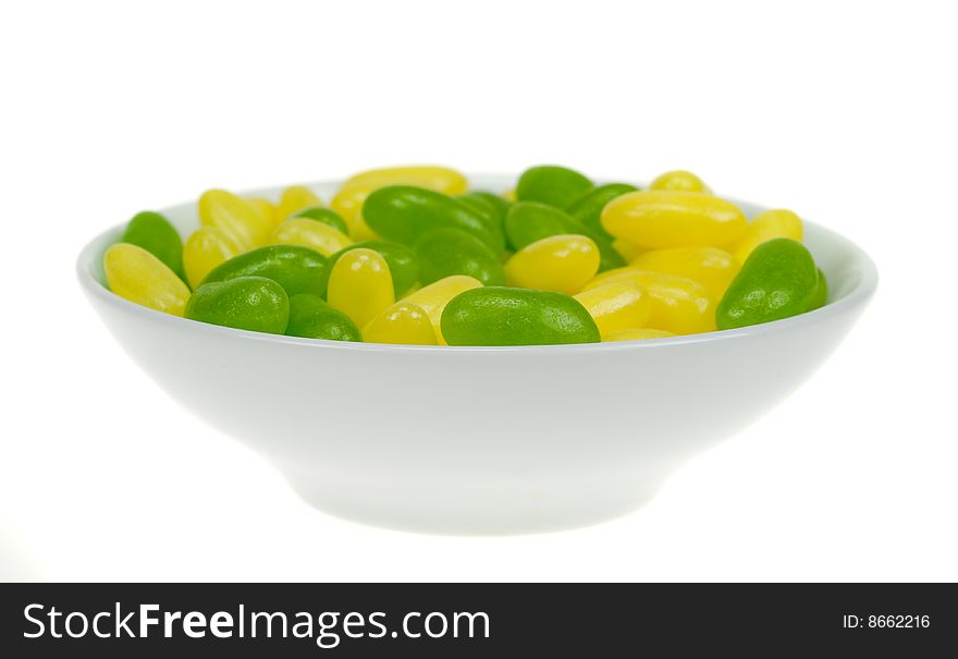 A bowl of green and yellow jelly beans isolated on a white background