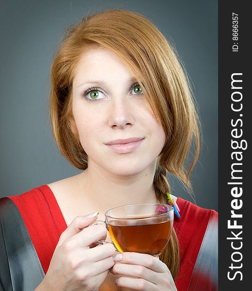 Redheaded girl with cup of tea on grey background