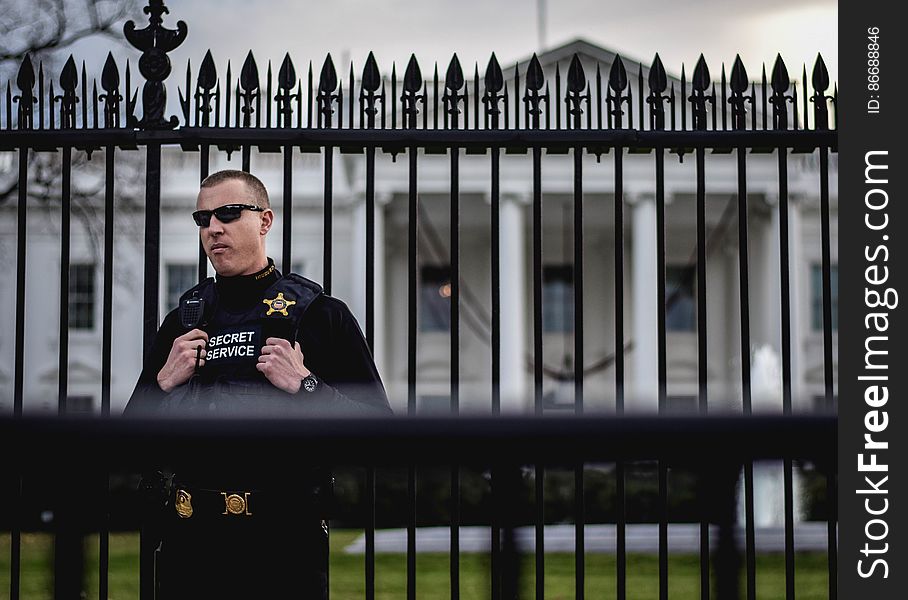 A United States Secret Service agent stands guard between the upgraded security fence and metal barricade &#x28;foreground&#x29; that block off the north lawn of the White House from tourists on Pennsylvania Avenue NW on December 13, 2015. Released into the public domain under a CC0 license. A United States Secret Service agent stands guard between the upgraded security fence and metal barricade &#x28;foreground&#x29; that block off the north lawn of the White House from tourists on Pennsylvania Avenue NW on December 13, 2015. Released into the public domain under a CC0 license.
