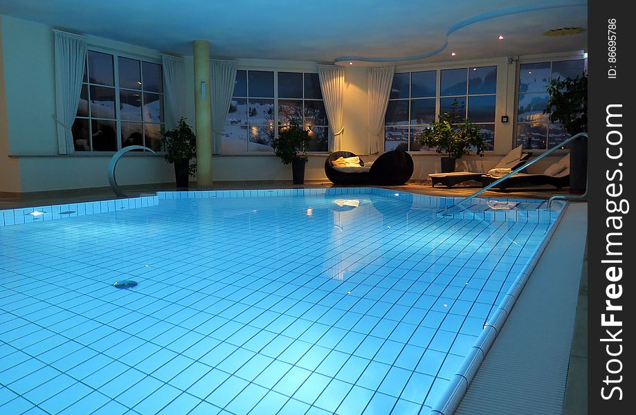 Empty indoor swimming pool with lounge chairs illuminated at night.