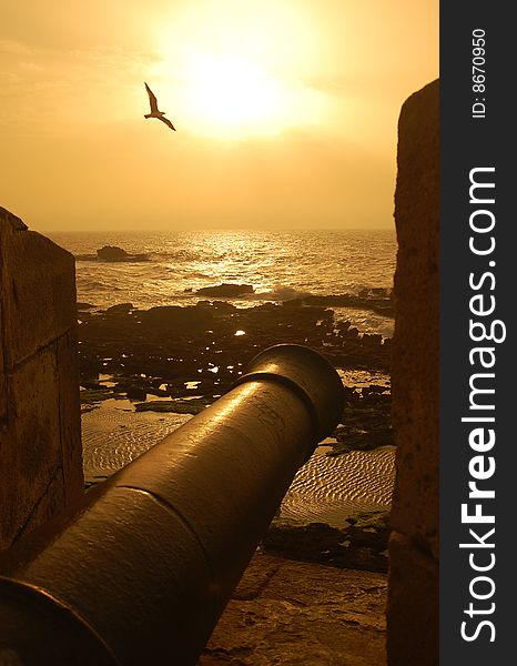 The sun sets through a crenelation of the Portuguese fort in Essaouira, Morocco. The sun sets through a crenelation of the Portuguese fort in Essaouira, Morocco.