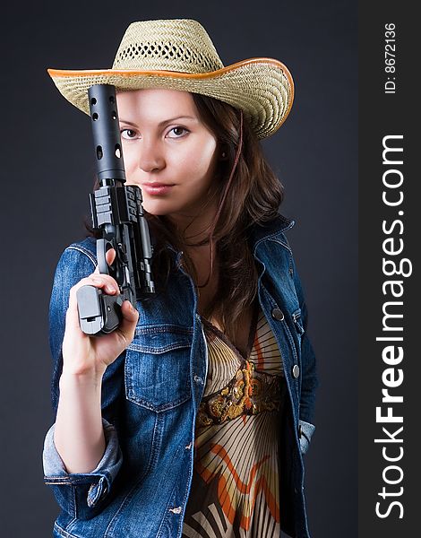 Girl in a cowboy's hat with the big pistol against a dark background. Girl in a cowboy's hat with the big pistol against a dark background