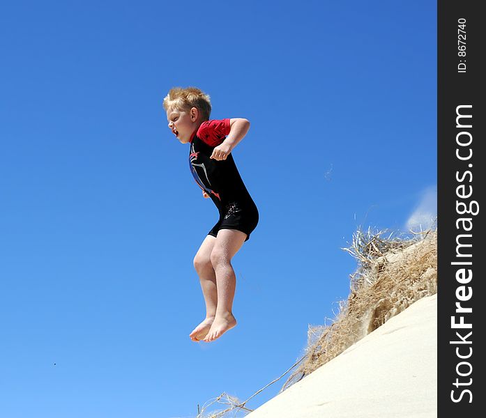 Boy jumping off sand dune