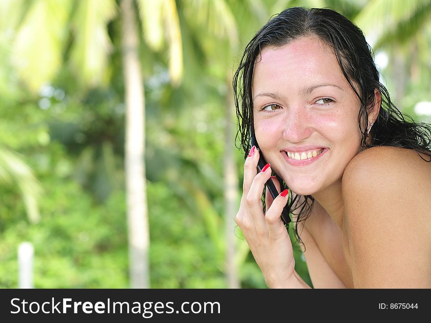 Beautiful young woman with big smile talking on the phone outdoors. Palm trees and paradise in the background. Beautiful young woman with big smile talking on the phone outdoors. Palm trees and paradise in the background.